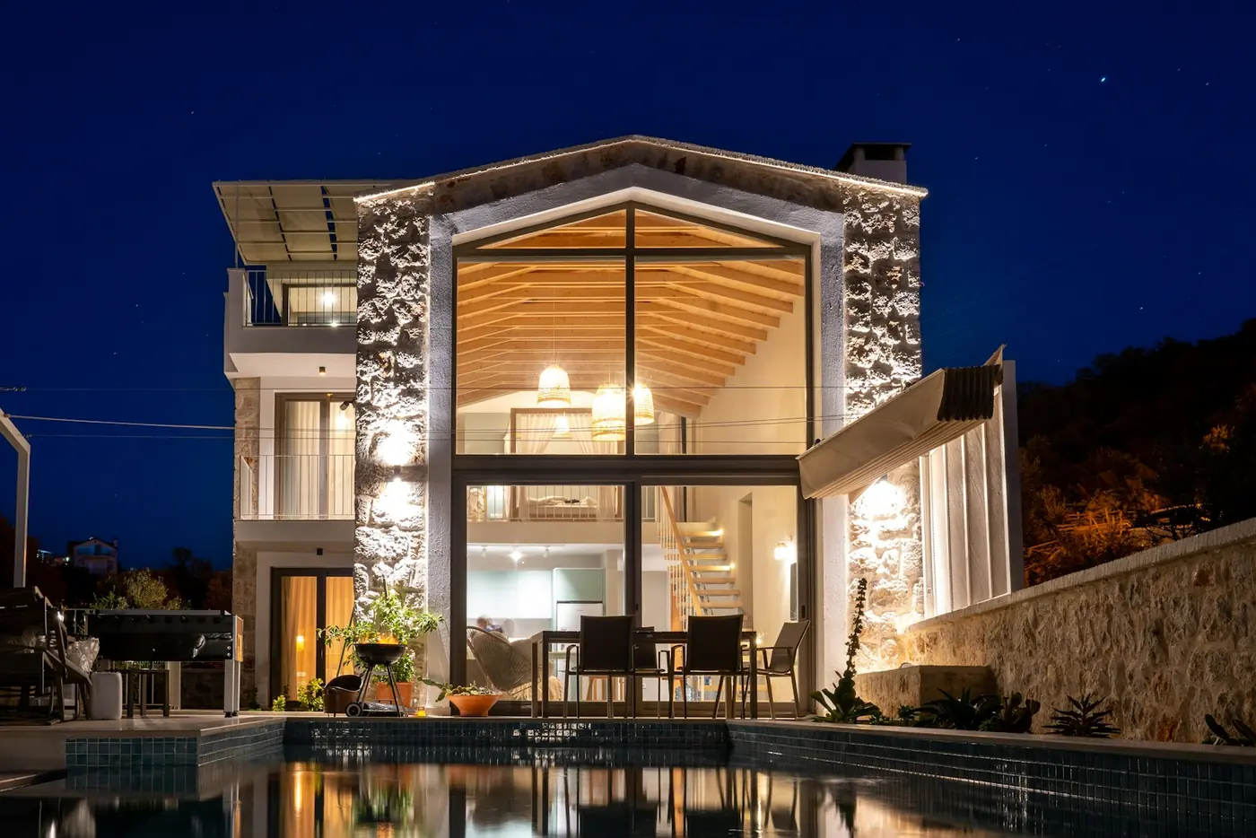 Taş cepheli, kırma çatılı, büyük cam pencereli villa ve önünde havuz